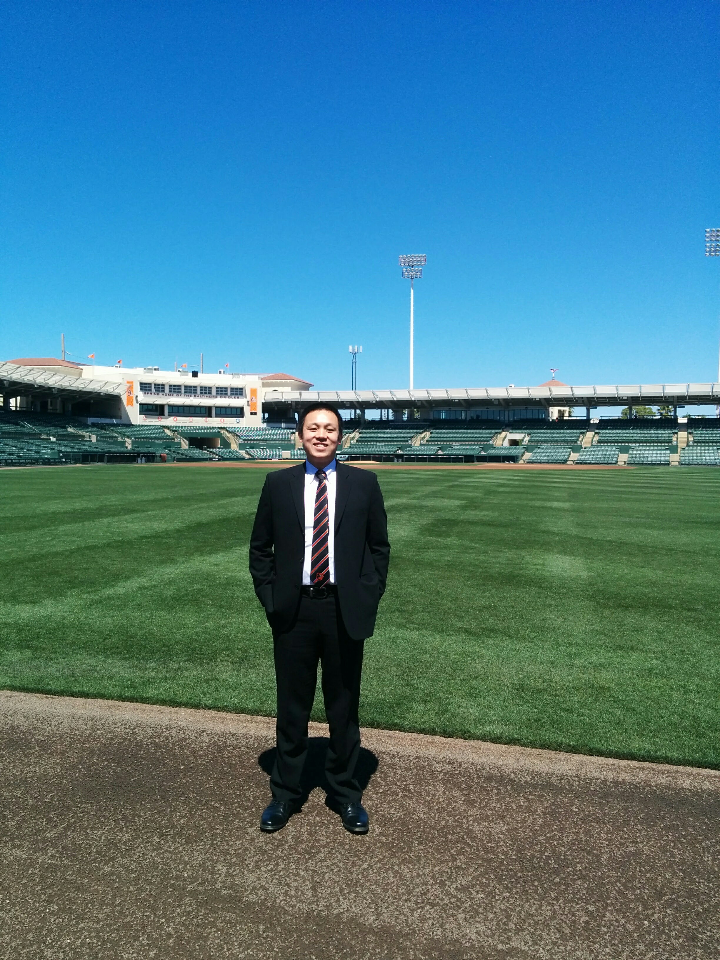 Di Zou standing on a baseball field in a suit