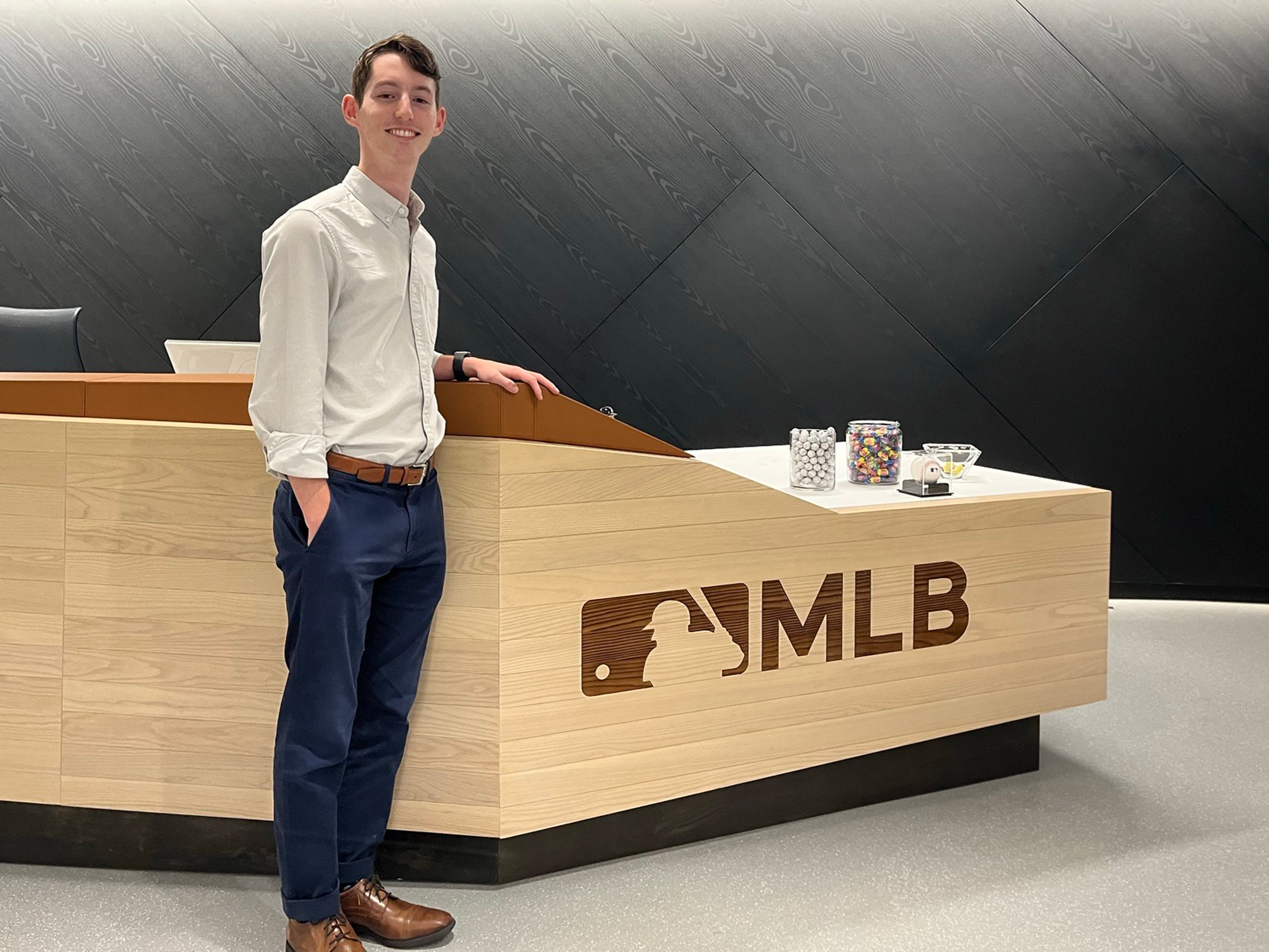 Josh Leeman standing in front of Major League Baseball desk