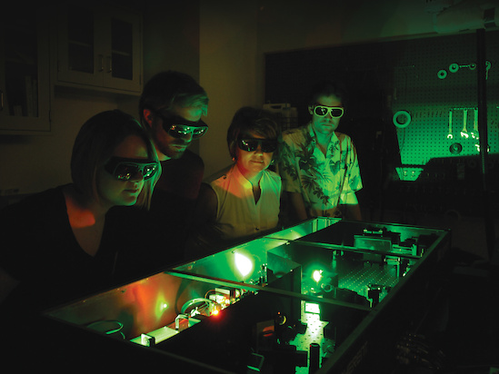 (L-R) Chemistry graduate students Hannah Ogden and Paul Diss, Professor Amy Mullin and Intern Augustus Cooke-Nesme (University College London) inspecting their laser system that generates highly excited molecules. Photo: (L-R) Chemistry graduate students Hannah Ogden and Paul Diss, Professor Amy Mullin and Intern Augustus Cooke-Nesme (University College London) inspecting their laser system that generates highly excited molecules.